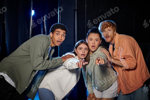 Preview: group of diverse astonished friends discovering a clue in escape room, women pointing with finger