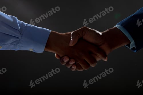 Preview: Mid section of two businessmen shaking hands against black background