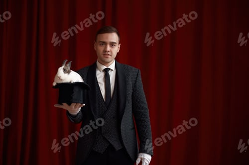Preview: Young handsome magician holding top hat with cute fluffy rabbit
