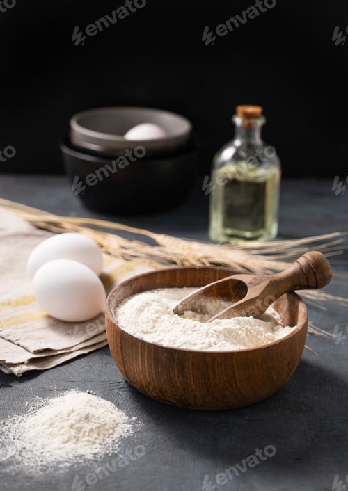 Preview: Wheat flour in a wooden bowl with a scoop on a dark blue background with eggs,