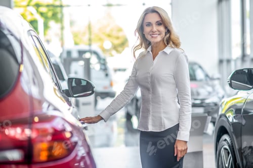 Preview: Smiling woman touching car door in dealership
