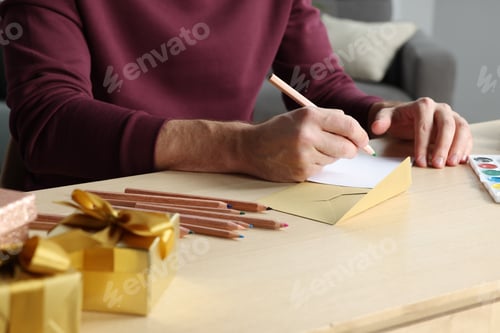 Preview: Man writing message in greeting card at wooden table, closeup