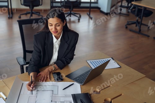 Preview: Smiling female architect engineer working with documents project sitting desk in office