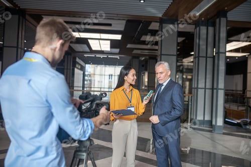 Preview: Asian female reporter standing next to grey-haired man