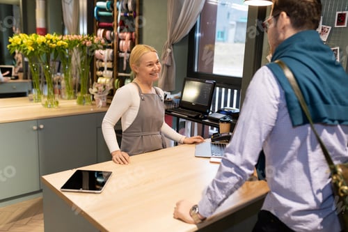 Preview: an employee of a flower shop kindly meets a client at the work counter