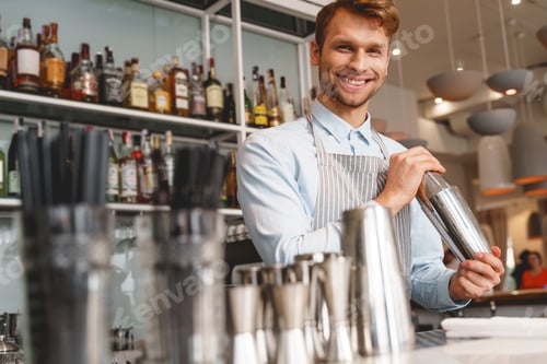 Preview: Cheerful bartender in apron mixing cocktail with shaker