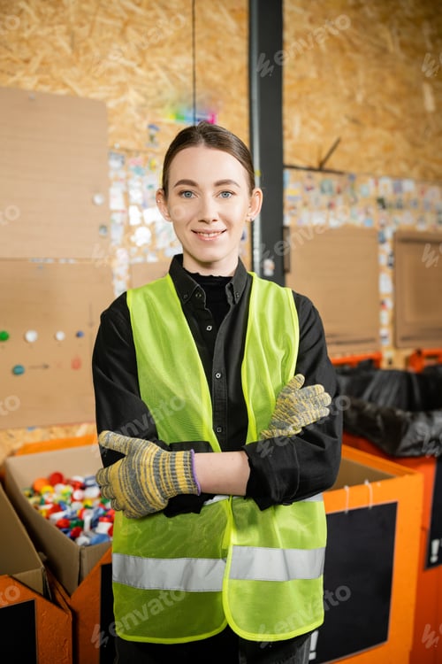 Preview: Smiling worker in high visibility vest and gloves looking at camera and crossing arms