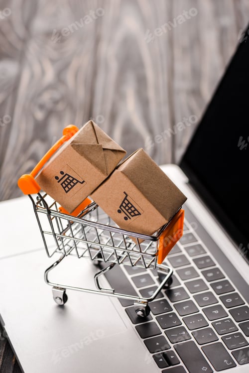 Preview: selective focus of toy carton boxes in small shopping cart on laptop with blank screen, e-commerce