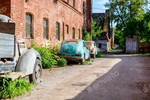 Preview: an Old rusty and abandoned retro car covered by green plants, outside