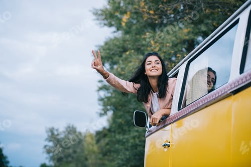 Preview: happy attractive girl showing peace symbol white traveling in retro minivan