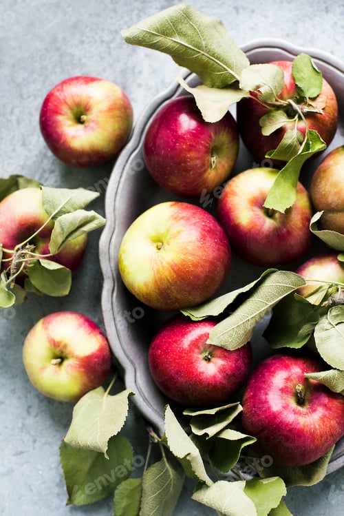 Preview: A bowl of fresh, red apples with leaves on a textured surface