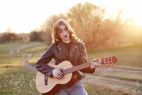 Preview: Beautiful girl playing guitar at sunset around spring nature