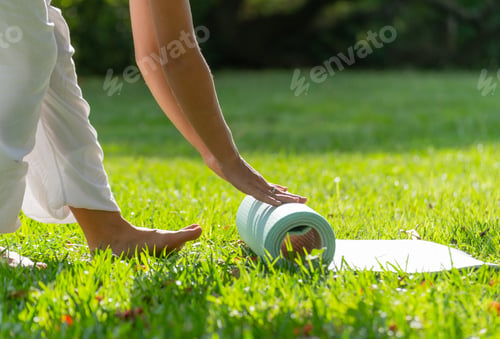 Preview: Young Woman Rolling Yoga Mat in a Green Park on a Sunny Day.Copy Space.Healthy Concept