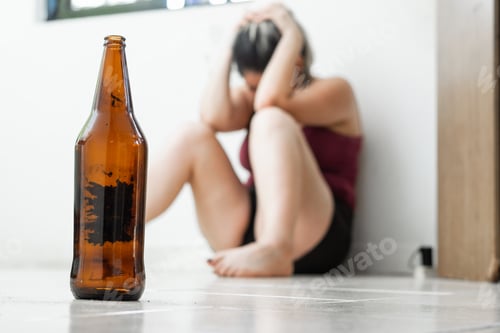 Preview: close-up of an empty beer bottle, placed on the ground, in the background a woman sitting