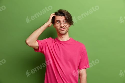 Preview: Horizontal shot of thoughtful handsome young European man scratches head looks doubtfully aside has