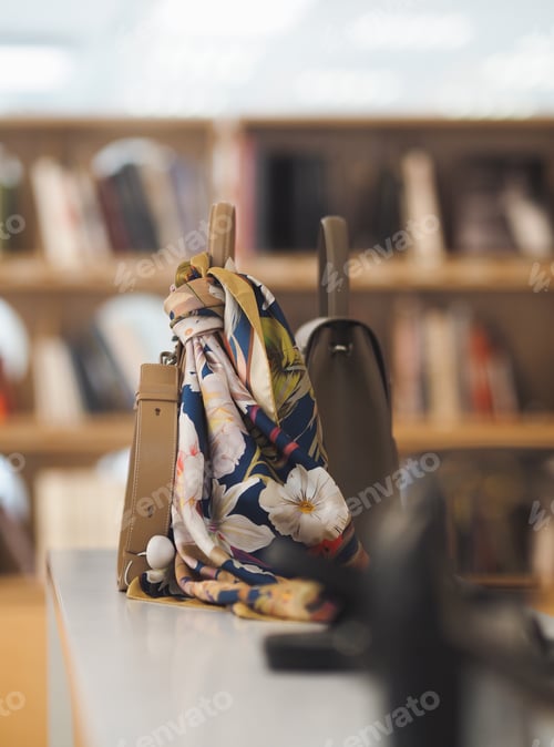 Preview: Designer bags with a colorful silk scarf stand on a shelf in a luxury boutique, no people.