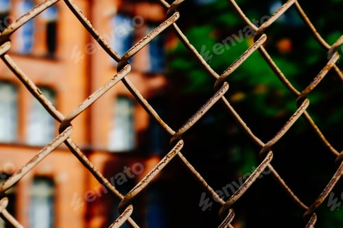 Preview: Metal fence in front of a building next to a tall green tree