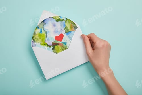 Preview: top view of woman holding envelope with planet picture on turquoise background, earth day concept