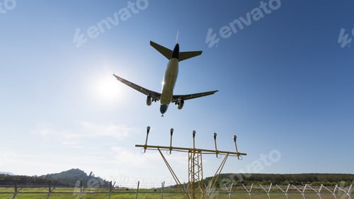 Preview: Airplane with chassis flying overhead against blue sky landing light leading to runway on background