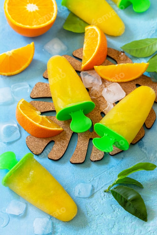 Preview: Homemade popsicles with orange juice, fruit ice, lollipops on a blue stone or slate background.