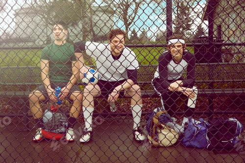 Preview: Portrait of three male soccer players sitting behind wire fence