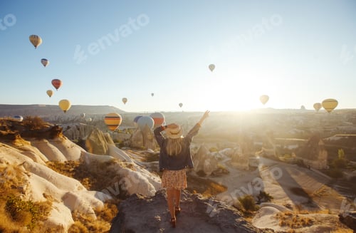 Preview: Young attractive girl stands on mountain with flying air balloons. View from the back. Cappadocia.