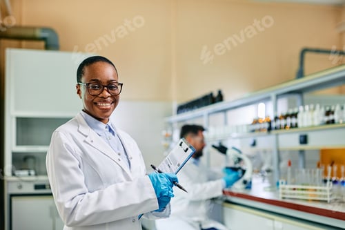 Preview: Happy black female biotechnologist working in lab and looking at camera.