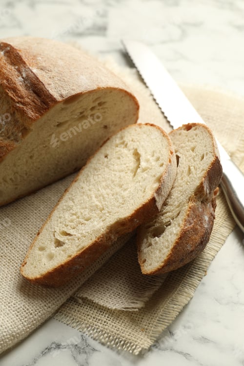 Preview: Pieces of fresh bread and knife on white marble table, closeup