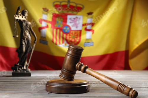 Preview: Judge's gavel and statue of Lady Justice on wooden table against flag of Spain, closeup