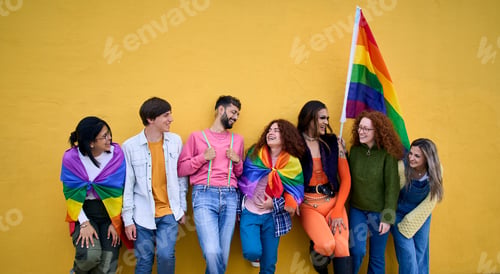 Preview: Group of diverse LGBT young people standing on wall yellow. Smiling friends celebrating gay pride