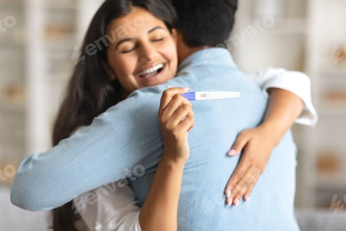 Preview: Indian woman joyfully hugging man, holding positive pregnancy test