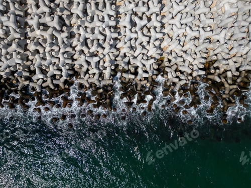 Preview: Aerial view of concrete tetrapod wave breakers along a rugged shoreline, with waves crashing against