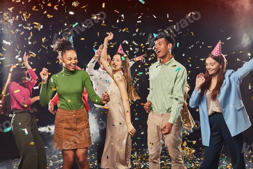 Preview: Group of young happy multiracial people wearing birthday hats dancing and having fun, confetti