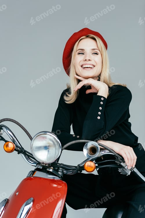 Preview: Stylish pretty woman in black clothes posing by red motorcycle isolated on grey