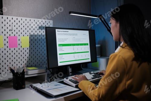 Preview: Pretty happy young entrepreneur woman working with laptop sitting in the office at night.