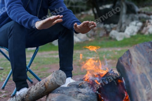 Preview: Adult Warming Hands by Campfire in Nature