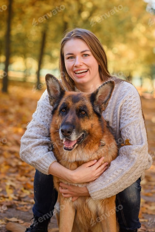 Preview: beautiful happy girl in a sweater and jeans with a dog girl with a shepherd dog in the park in the f