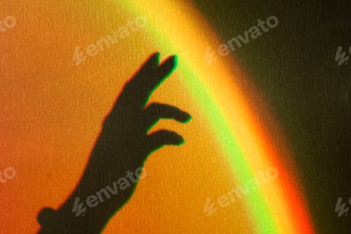 Preview: Shadow of womans hand. Rainbow reflection of sunbeam on wall. Hand touches rainbow.