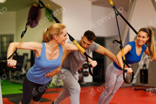 Preview: Personal trainer assisting young woman while exercising with trx in the gym