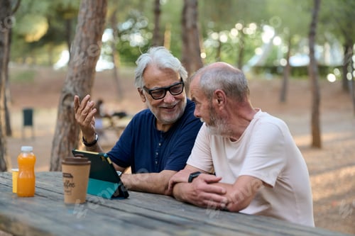 Preview: Two senior men using tablet in park, enjoying digital life