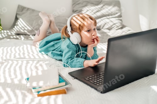 Preview: Emotional cheerful baby girl in headphones at home with a laptop, online training for a preschooler,
