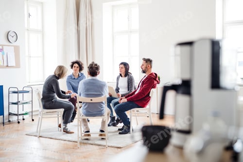 Preview: Men and women sitting in a circle during group therapy, talking.