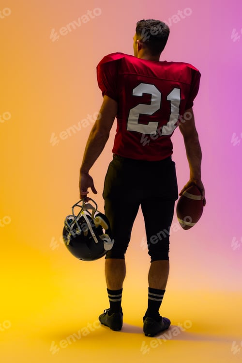 Preview: Caucasian male american football player holding helmet and ball with neon yellow and purple lighting