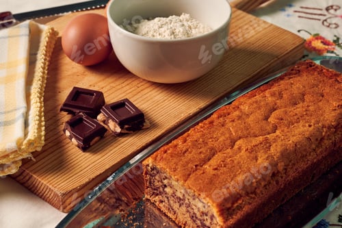 Preview: Homemade sponge cake on a white tablecloth with some ingredients: eggs, chocolate and flour.