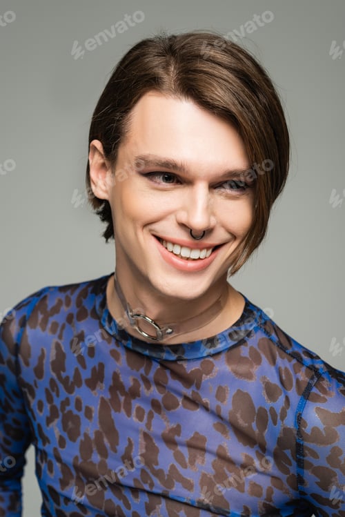 Preview: portrait of stylish and joyful pangender person with makeup and nose piercing isolated on grey