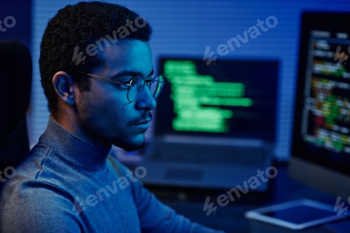 Preview: Young serious IT support engineer in eyeglasses looking at computer screen