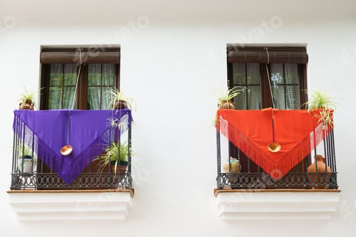 Preview: Two balconies with colorful drapes, plants, and pots on a white building facade