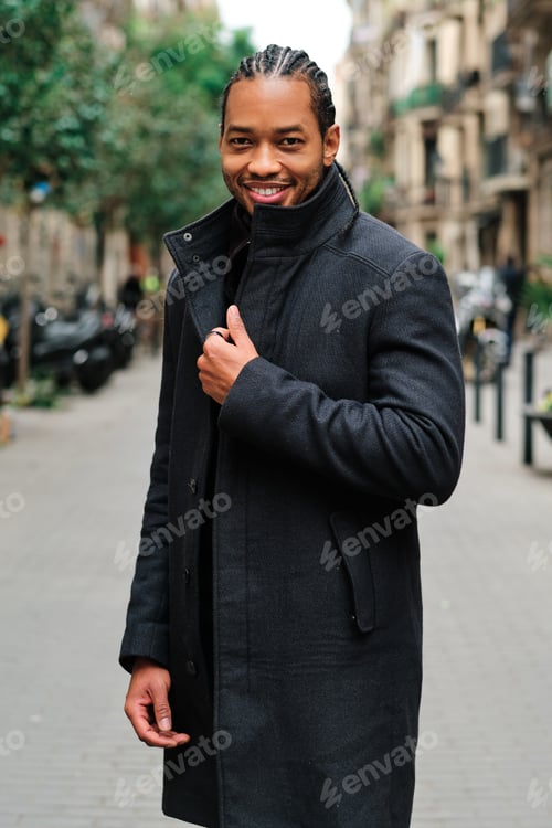 Preview: Confident and stylish African American man looking at camera and smiling while posing outdoors on