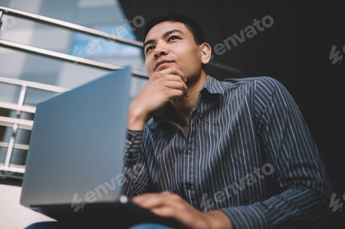 Preview: Asian millennial guy using laptop on stairs