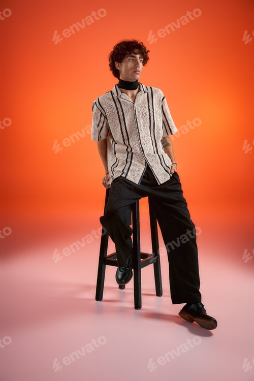Preview: Stylish young man poses confidently against a vibrant orange backdrop in modern fashion